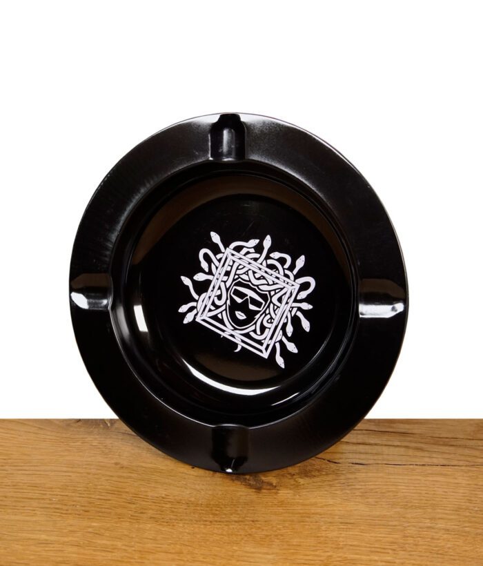 Schwarzer Aschenbecher mit weißem Medusa-Design auf Holzuntergrund.