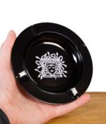Schwarzer Aschenbecher mit Medusa-Motiv wird in einer Hand präsentiert.