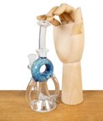 Glaspfeife mit blauer Perkolator-Kammer, daneben eine Holzhand zur Größenreferenz.