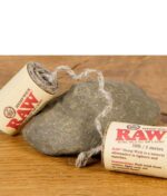 RAW Hemp Wick Rolle mit abgewickeltem Docht und Anwendungshinweisen auf der Verpackung, dekorativ auf Stein.