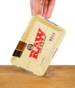 RAW Classic Mini Rolling Tray mit typischem RAW-Design, von Hand über einem Holztisch gehalten.