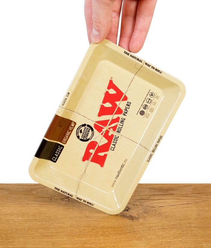 RAW Classic Mini Rolling Tray mit typischem RAW-Design, von Hand über einem Holztisch gehalten.