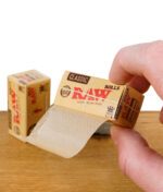 RAW Classic Rolls Kingsize Slim, ungebleichtes Endlos-Rollpapier, von Hand gehalten mit Verpackung auf Holztisch.