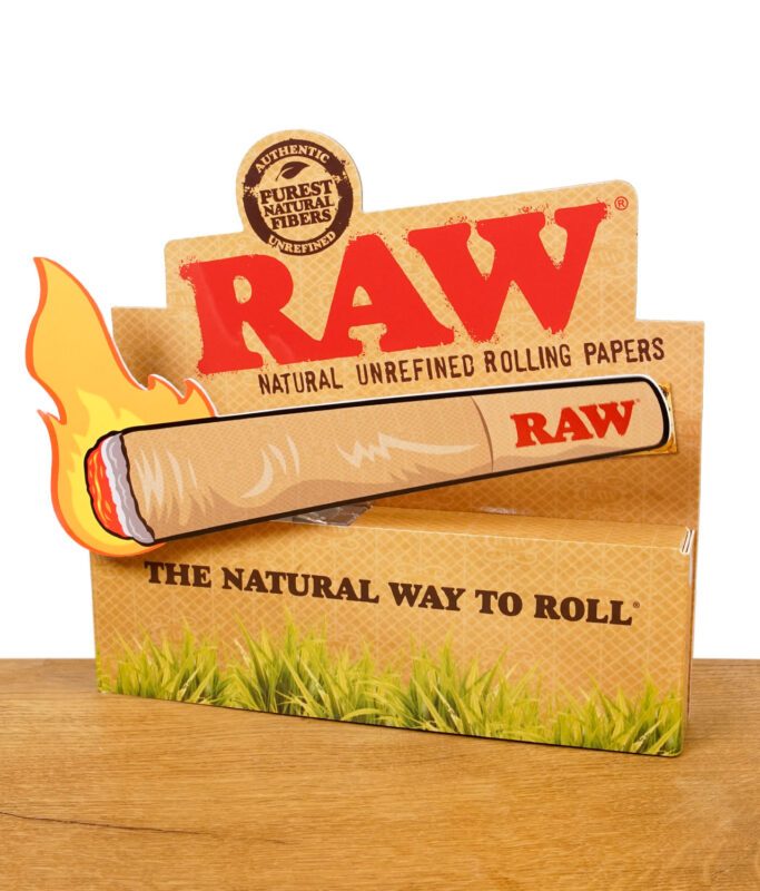 RAW Aufsteller aus Pappe mit Feuer-Design und Slogan 'The Natural Way to Roll' auf Holztisch