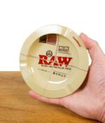 Hand hält RAW Aschenbecher aus Metall im RAW Classic Rolling Papers Look