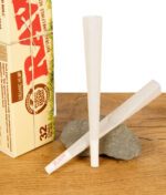 Zwei RAW Organic Hemp Cones King Size aus dem 32er Pack vor der Verpackung auf Naturstein und Holzoberfläche