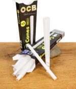 Geöffnete Verpackung der OCB Premium Cones Slim 3er Pack mit drei vorgedrehten Cones auf Holz- und Steinuntergrund
