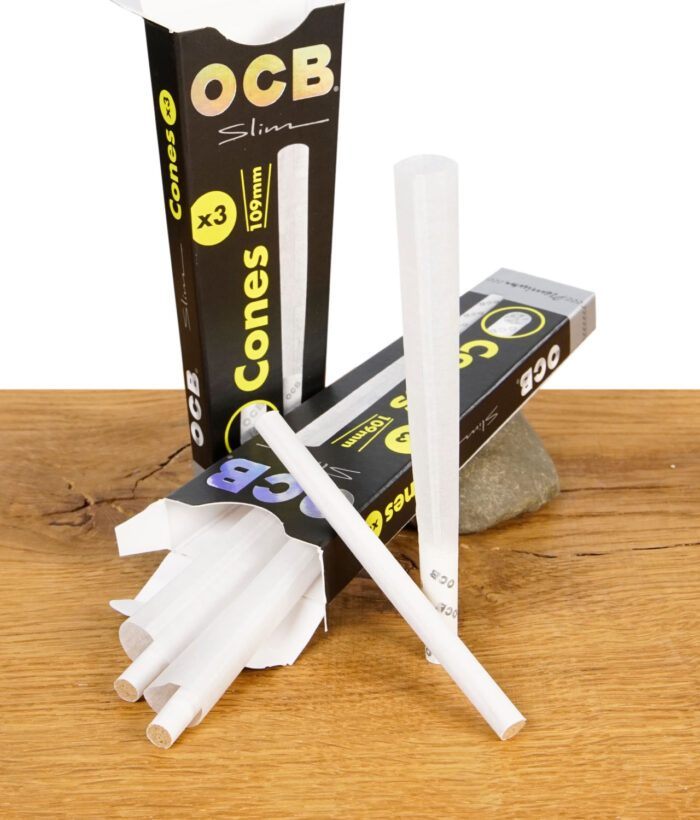 Geöffnete Verpackung der OCB Premium Cones Slim 3er Pack mit drei vorgedrehten Cones auf Holz- und Steinuntergrund