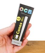 OCB Premium Cones Slim 3er Pack in schwarzer Verpackung, gehalten in einer Hand über Holztisch