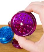 Black Leaf Grinder Acryl 60mm in Lila, geöffnet und in der Hand gehalten, weitere Farben im Hintergrund
