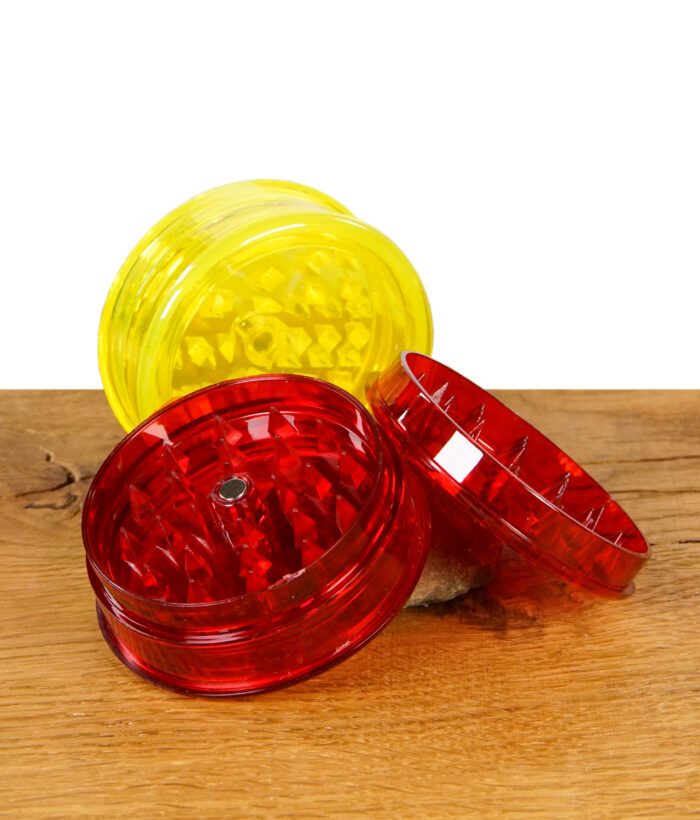 Black Leaf Grinder Acryl 60mm in Gelb und Rot, geöffnet und mit Mahlwerk sichtbar auf Holztisch