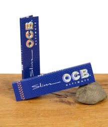 Zwei geschlossene Packungen der OCB Ultimate Slim Papers King Size mit holografischem Logo auf blauem Hintergrund.