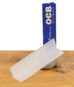 Einzelnes OCB Ultimate King Size Slim Paper vor der stehenden Verpackung, ultradünn und leicht transparent.