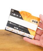 Hand hält eine geöffnete Packung OCB Premium Slim + Filters mit weißen Filtertips und einem einzelnen ungebleichten Papier.