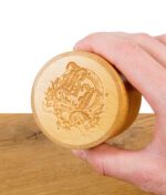 Hand hält den runden Bambusdeckel des Black Leaf Grinders mit eingraviertem Logo.
