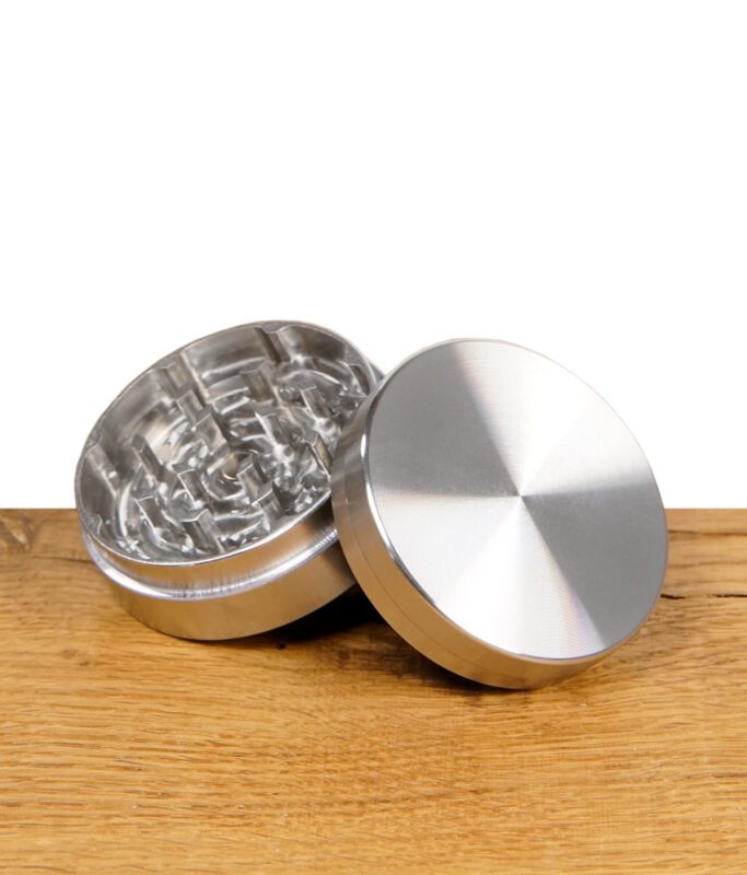 Geöffneter silberner Grinder aus Metall mit scharfen Mahlzähnen auf Holzoberfläche.
