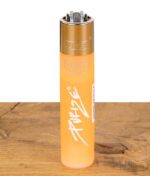 Orangefarbenes Clipper Feuerzeug mit Purize Logo stehend auf Tischplatte