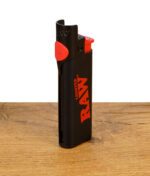 RAW Phoenix Clipper Lighter mit rotem Logo und integriertem Stopfwerkzeug auf Holztisch