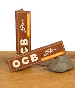 Zwei geschlossene Packungen OCB Virgin Paper King Size Slim ungebleicht auf Holztisch mit Stein als Stütze