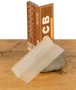 Ein einzelnes ungebleichtes OCB Virgin Rolling Paper in Regular Size vor der Rückseite der Verpackung auf einem Stein