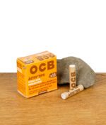 OCB Activ'Tips Extra Slim im 15er Pack, ungebleicht – geschlossene Verpackung mit zwei Aktivkohlefiltern vor Stein auf Holztisch