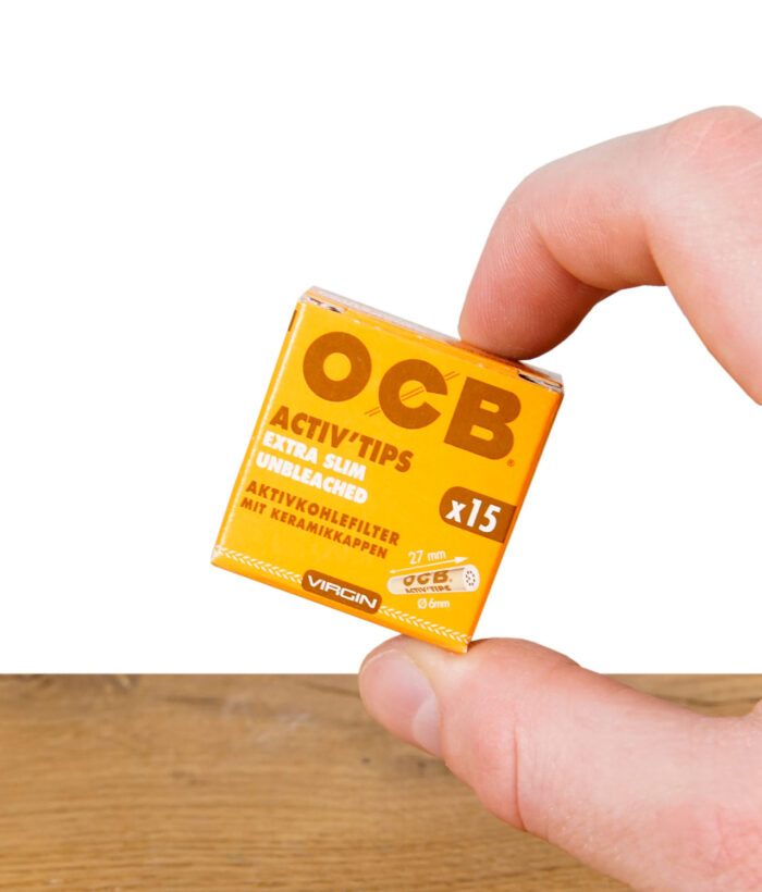 Kleine Schachtel OCB Activ'Tips Extra Slim 15er Pack ungebleicht, zwischen zwei Fingern gehalten – Vorderseite sichtbar
