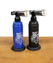 Zwei Black Leaf Butangasbrenner mit Triple-Jet-Flamme, in Blau und Schwarz, stehend nebeneinander auf Holztisch