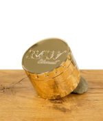 RAW Ethereal Grinder goldfarben, geschlossen, aufrecht geneigt auf Stein – mit RAW-Logo auf dem Deckel