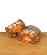 Zwei geschlossene Packungen OCB Virgin Paper Rolls Slim auf einem Holzuntergrund mit Stein
