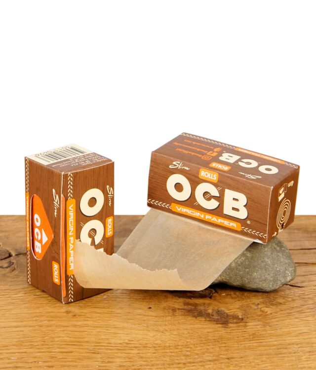 OCB Virgin Paper Rolls Slim mit herausgezogener Papierbahn, beide Packungen nebeneinander auf Holz mit Stein