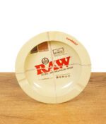RAW Aschenbecher aus Metall mit typischem RAW Classic Design, stehend auf einem Holztisch