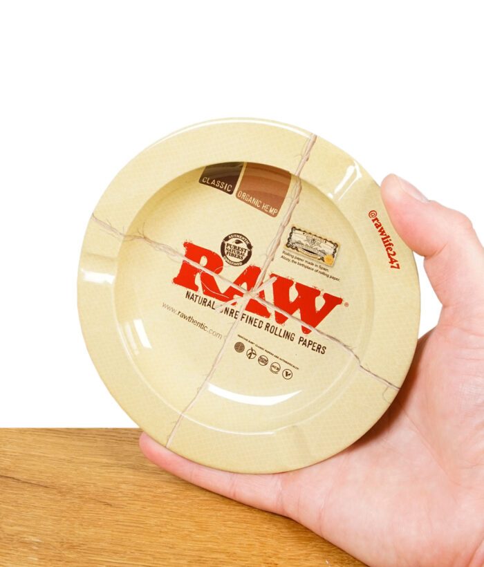 Hand hält den runden RAW Magnet-Aschenbecher mit beige-rotem Design und Kordelaufdruck
