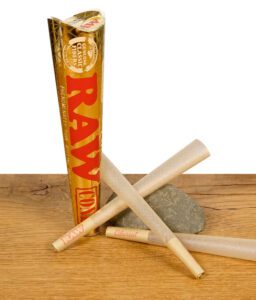 Drei RAW Ethereal Cones mit goldener Verpackung auf einem Holzuntergrund, zwei auf einem Stein liegend.