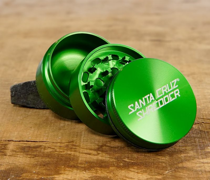 Grinder mit oder ohne Sieb? HJier ist ein Grüner Santa Cruz Shredder Grinder ohne Sieb, geöffnet auf einer Holzfläche zu sehen
