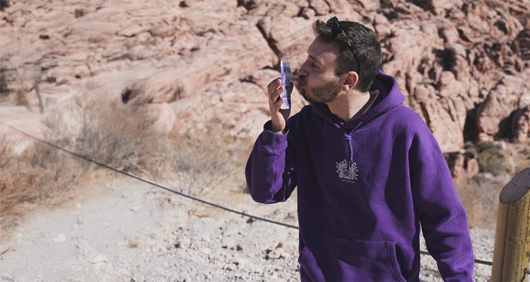 Mann im lila Hoodie küsst ein violettes Medusafilters-Pack vor einer Felskulisse