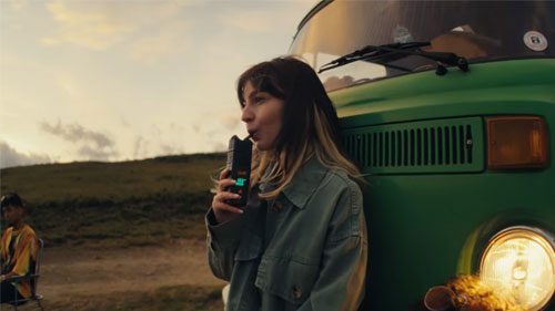 Frau nutzt unterwegs einen tragbaren Vaporizer mit viel Dampf von Storz & Bickel neben einem grünen Van in der Natur.