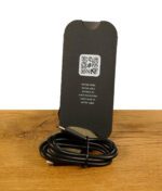 Puffco New Peak Ladekabel in Schwarz mit QR-Code-Karte auf Holz mit Stein im Hintergrund.