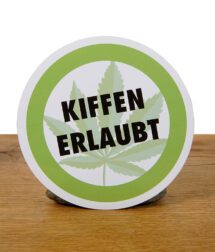 Runder „Kiffen erlaubt“ Aufkleber aufrecht stehend auf Holzuntergrund mit grünem Rand und Hanfblatt