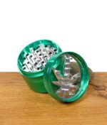 Grüner Grinder geöffnet, Deckel mit Hanfblattmuster liegt seitlich vor dem Mahlwerk