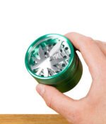 Hand hält grünen Grinder mit silbernem Hanfblatt-Einsatz fest