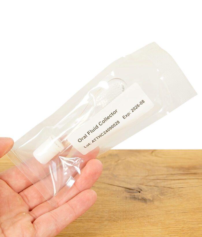 CleanU Speicheltest Oral Fluid Collector in einer Hand gehalten vor einem Holzbrett