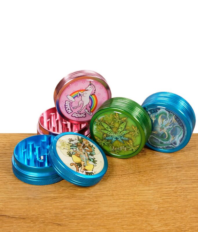 Vier Black Leaf Grinder mit bunten Motiven, teilweise geöffnet, auf Holztisch gruppiert