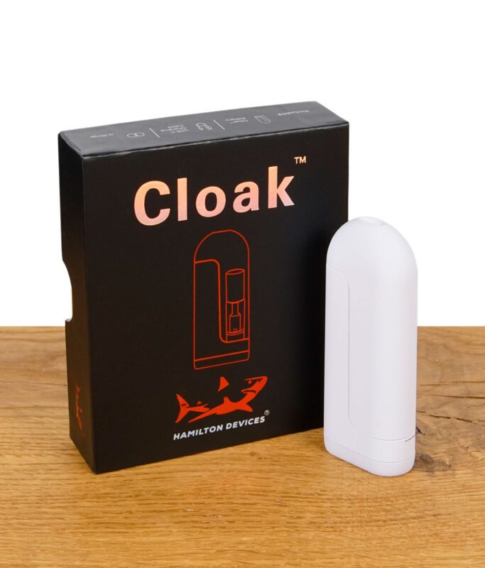 Weißer Cloak Vaporizer stehend vor schwarzer Verpackung mit oranger Grafik