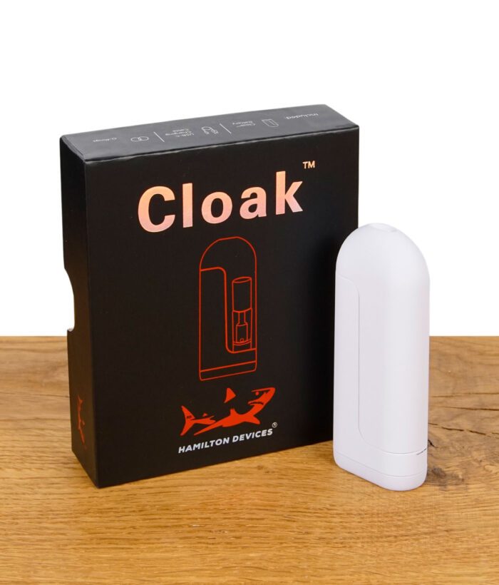 Weißer Cloak Vaporizer stehend vor schwarzer Verpackung mit oranger Grafik
