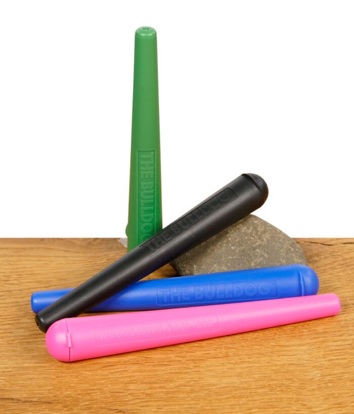 Vier THE BULLDOG Jointtubes in Grün, Schwarz, Blau und Pink auf einem Stein liegend, auf Holzoberfläche.