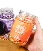 Hand hält Glas mit 500 Medusafilters der Sunset Edition in Orange, im Hintergrund Violet Edition sichtbar.