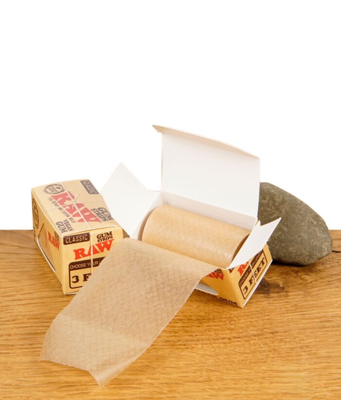 RAW Classic Gum Strips Rolle ragt aus geöffneter Verpackung neben einer zweiten Packung auf Holzoberfläche
