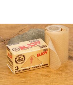 RAW Classic Gum Strips Rolle neben der geschlossenen Verpackung auf Holzuntergrund