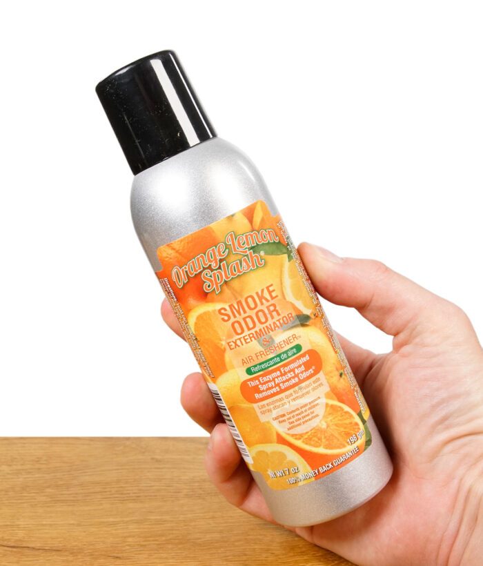 Hand hält Smoke Odor Exterminator Spray Orange Lemon Splash mit Blick auf das Etikett