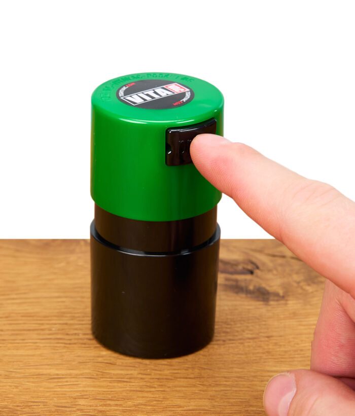 Finger betätigt Push-Button eines grünen Tightpac Vitavac Behälters auf Holztisch